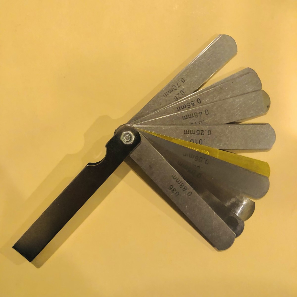 Feeler gauge, with its leaves fanned out, on table